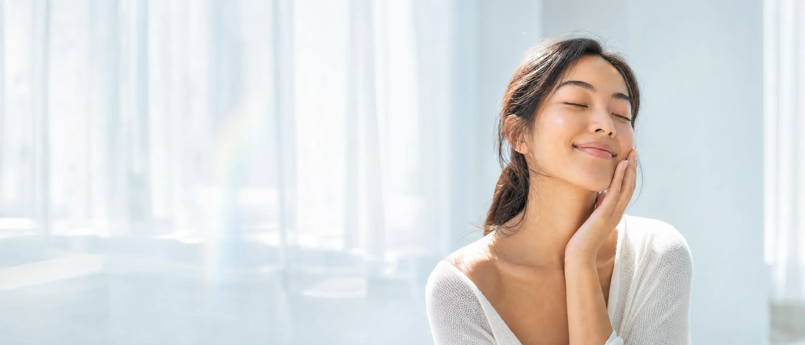 Woman with glowing skin smiling with her eyes closed in soft morning light
